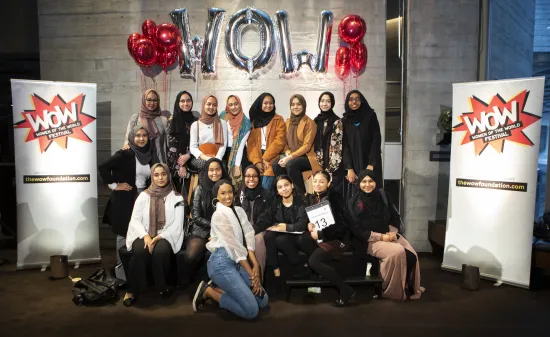 Girls from a school pose for a photo in front of balloons that spell out WOW
